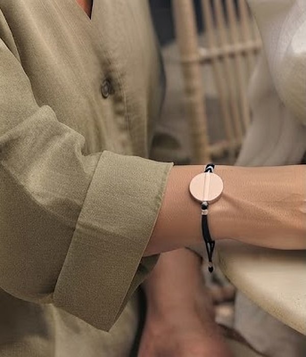 A friend's wrist in a sage linen sleeve wearing The Cord: a black silk cord with the Juni Charm