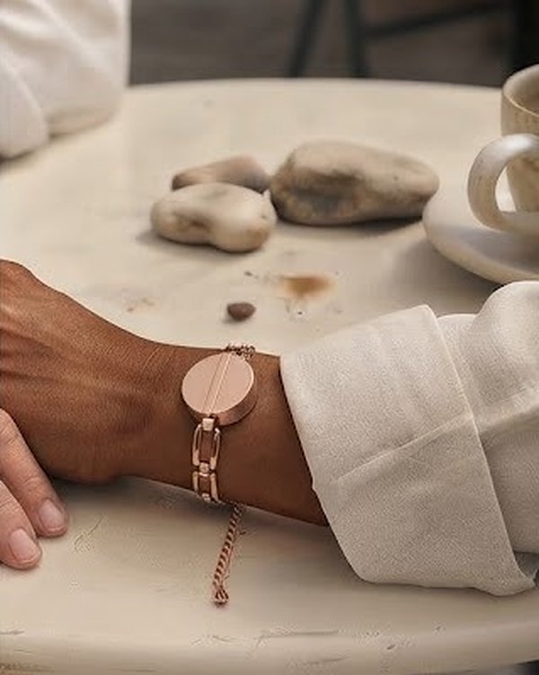 A wrist in a white linen sleeve wearing The Flex: a rose-gold link bangle with the Juni Charm